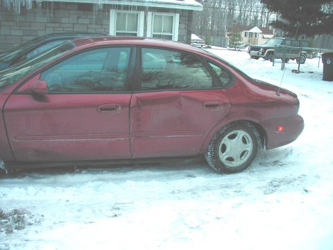 1997 Ford Taurus - A red sedan with a dented rear door sits in the snow, with another vehicle visible in the background.