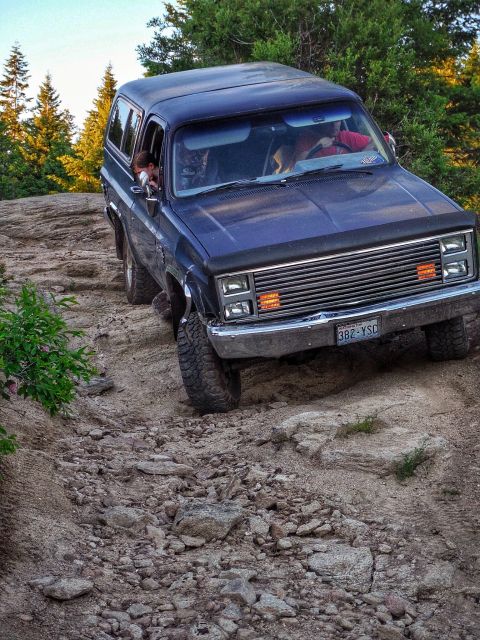 2005 Jeep Wrangler - A dark blue SUV is navigating a rocky, off-road trail with trees in the background. The front of the vehicle is angled towards the viewer,…