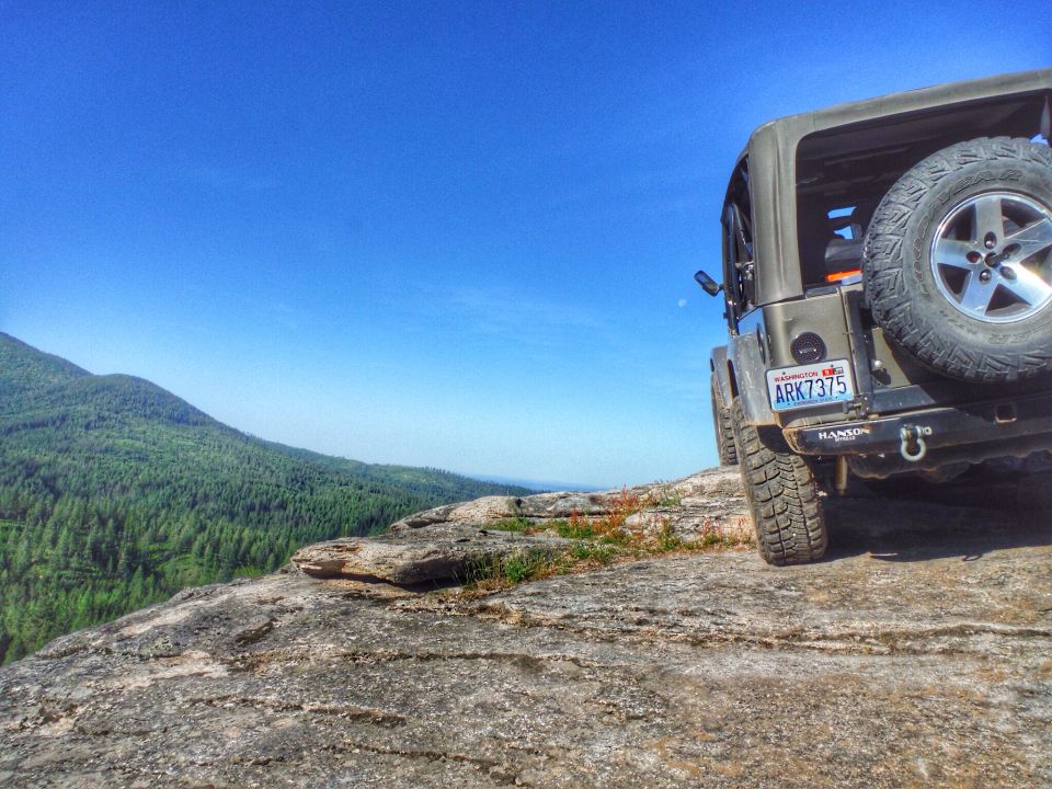 Rear view of a dark green Jeep Wrangler on a rocky overlook.