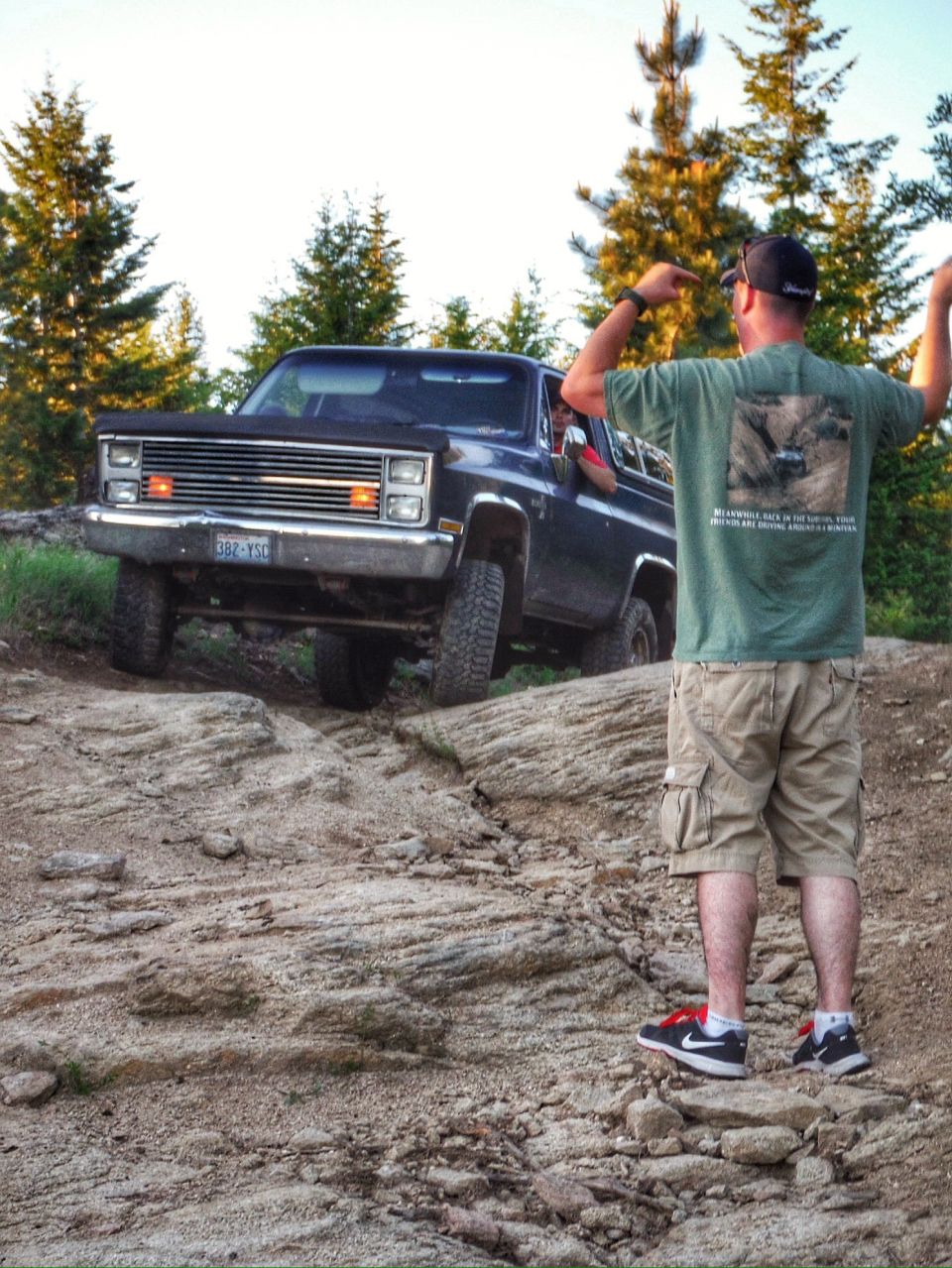 Dark blue SUV on a rocky trail with a man in a green t-shirt and khaki shorts standing behind it.