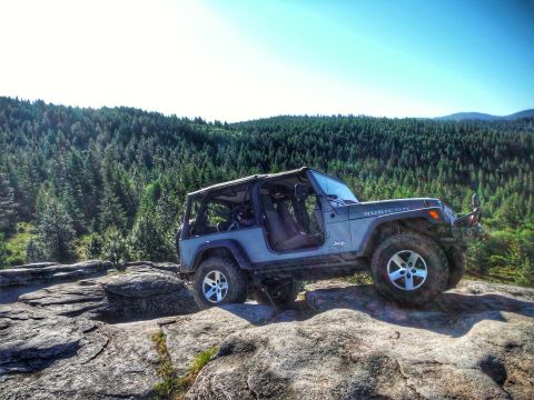 2005 Jeep Wrangler - A gray Jeep Wrangler Rubicon is parked on a rocky outcrop overlooking a dense forest. The top is removed, revealing the interior and roll c…