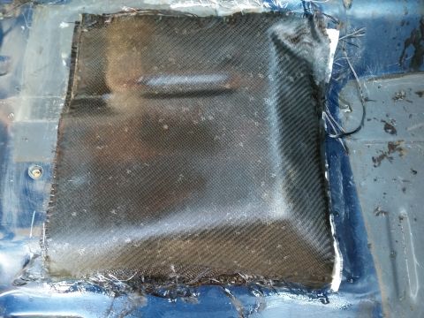 1988 Ford Bronco - A close-up view shows a patch of carbon fiber fabric being applied to a blue metal surface, likely a vehicle floor or body panel, with visi…