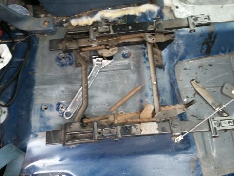 1988 Ford Bronco - The interior floor of a vehicle shows the removed seat mounting hardware, including rails and springs, with a wrench and knife resting on t…