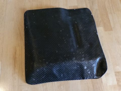 1988 Ford Bronco - A black carbon fiber part, possibly a fender flare or mud flap, is shown lying on a light-colored wooden floor. The part has a textured wea…