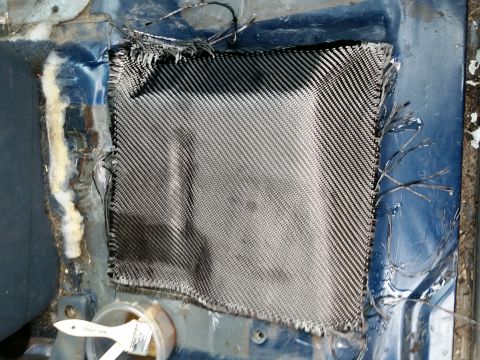 1988 Ford Bronco - A piece of carbon fiber fabric is being applied to a blue metal surface, likely a vehicle floor, with a brush and resin visible. The fabric…