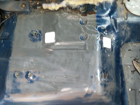 1988 Ford Bronco - The interior floor of a vehicle shows blue painted metal with some rust and dirt. Two small white squares are taped to the floor, possibly…