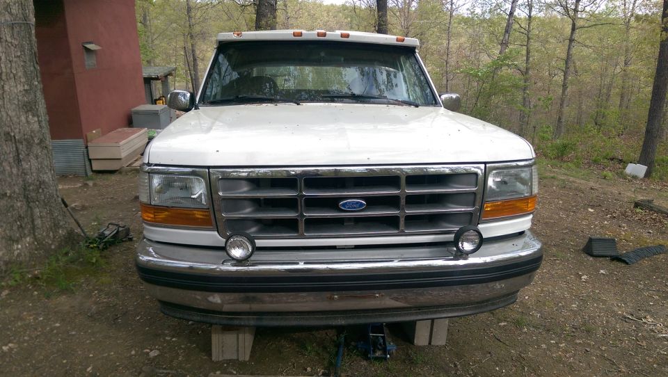 White Ford pickup truck front view, elevated on blocks, with chrome grille and auxiliary lights.