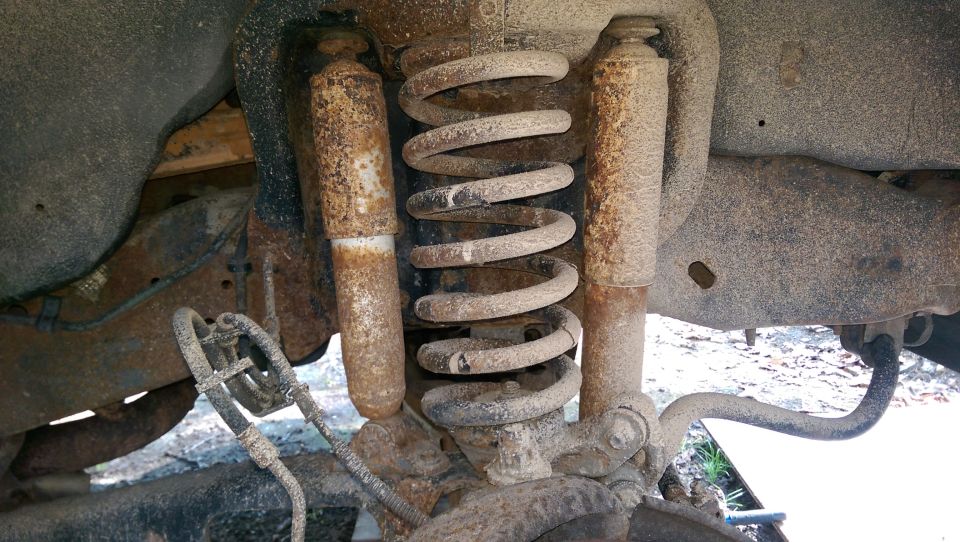Underside of a 1994 Ford Bronco showing rusty suspension with shock absorbers and coil spring.