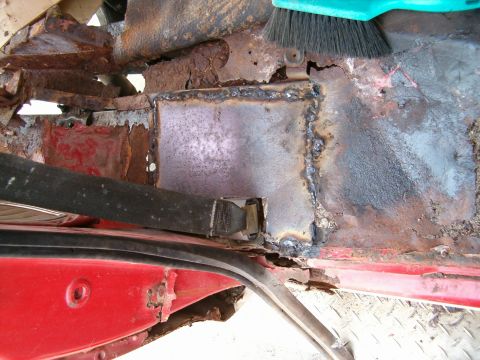 1979 Ford Bronco - Interior floor pan shows significant rust damage and a newly welded patch panel, with a seatbelt visible.