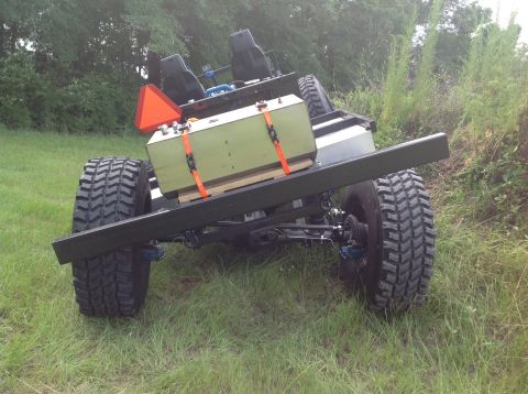 1992 Ford Bronco - The rear of a custom-built, four-wheeled vehicle with large off-road tires is shown. It features two black seats, a green fuel tank secured…