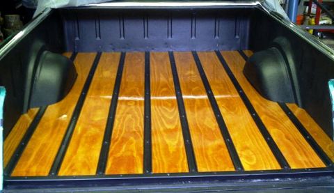 1971 Ford Ranchero - The wooden bed of a pickup truck features a glossy finish with black metal strips running lengthwise. The black wheel wells are visible on…