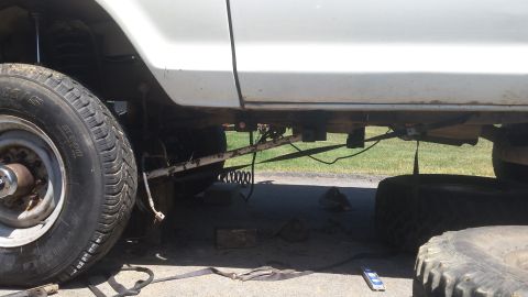 Undercarriage of a white Ford Bronco, front driver's side tire visible, on blocks.