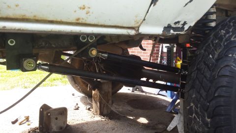Underside of a vehicle with modified suspension, showing control arms, tire, and frame.