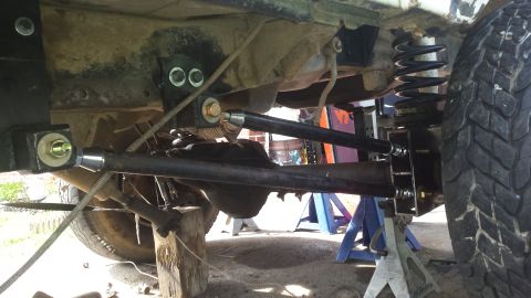 Underside of a vehicle with modified suspension, adjustable control arms, and coil springs on jack stands.