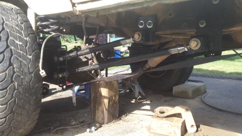 Underside of a vehicle showing rear suspension with adjustable control arms and a tire.