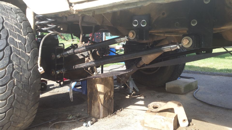 Underside of a vehicle showing rear suspension with adjustable control arms and a tire.