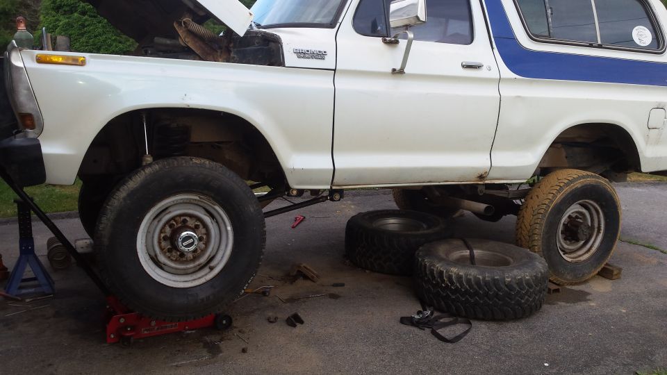 1979 Ford Bronco with front wheel removed, jacked up, with spare tires on the ground.