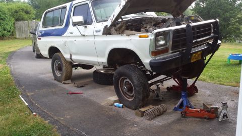 White 1979 Ford Bronco on jack stands, hood up, with coil spring removed.