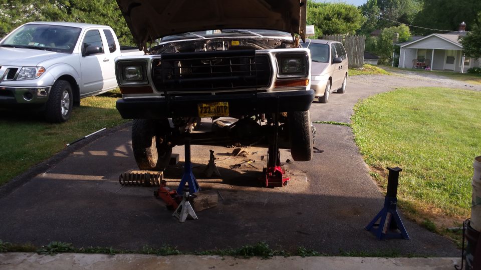 Lifted Ford Bronco on jack stands, hood open, with a Nissan Frontier nearby.