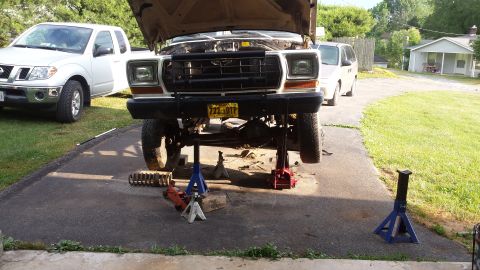 1979 Ford Bronco undergoing repairs in a driveway, with a Nissan pickup truck nearby.