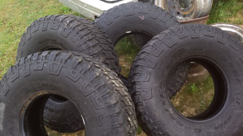 Four off-road tires piled on grass.