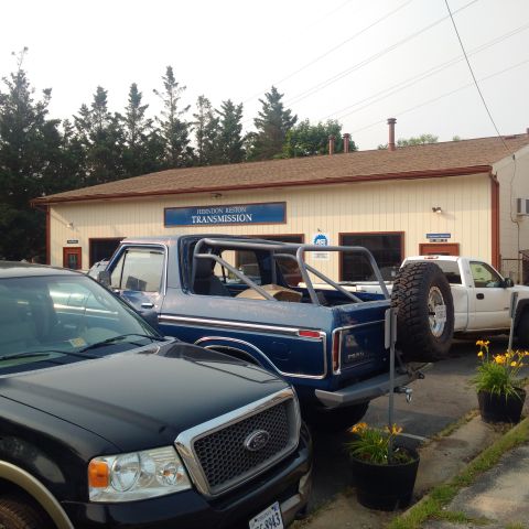 1978 Ford Bronco - A blue Ford Bronco with a roll cage is parked in front of a transmission shop. A black Ford F-150 is parked in the foreground.