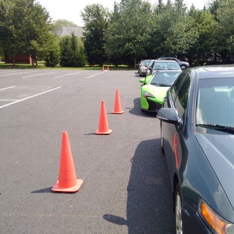 1978 Ford Bronco - A line of orange traffic cones is set up in a parking lot, with several cars parked behind them. A bright green sports car is visible in th…