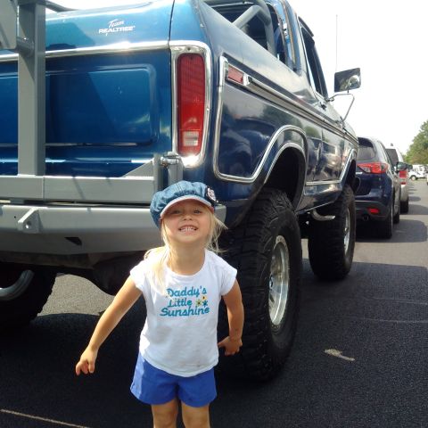 1978 Ford Bronco - A young girl in a denim hat and a white t-shirt that says "Daddy's Little Sunshine" poses in front of the rear of a lifted blue Ford Bronco…