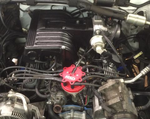 1993 Ford Bronco - This is a close-up, overhead view of a Ford Bronco engine bay, featuring a black intake manifold, a red MSD distributor cap, and various ho…