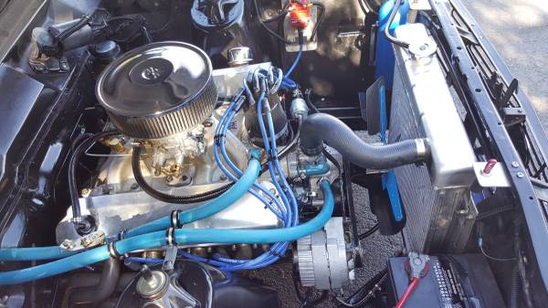 Close-up of a classic car engine bay with chrome air cleaner and blue spark plug wires.
