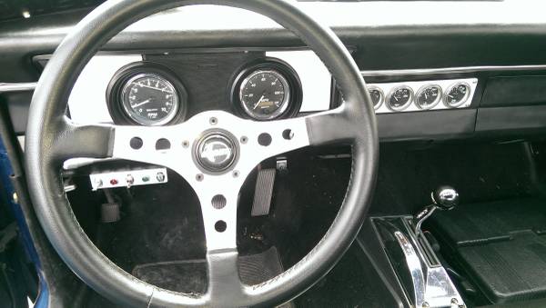 Interior view of a classic car dashboard with steering wheel, gauges, and shifter.