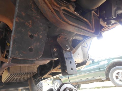 1994 Ford Bronco - Underside view of a heavily modified vehicle, likely a 1994 Ford Bronco, showing custom metal brackets and suspension components. A green v…
