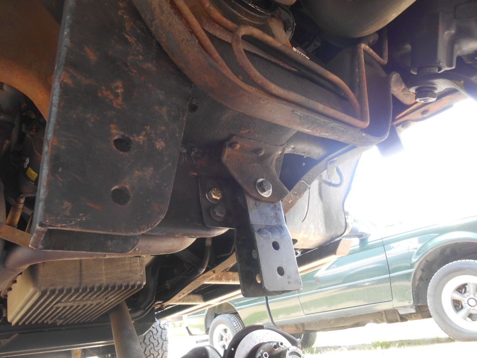 Underside of a modified vehicle with custom brackets and suspension. Green vehicle in background.