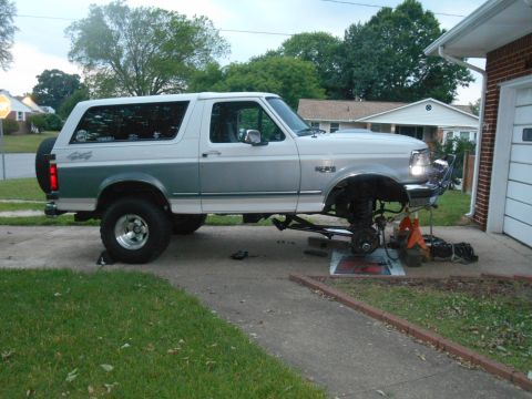1994 Ford Bronco - A two-tone white and green 1994 Ford Bronco is parked in a driveway with its front end raised on jack stands for maintenance. The vehicle h…