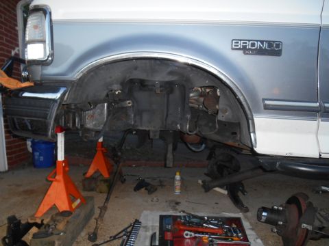 1994 Ford Bronco - The front passenger side of a lifted 1994 Ford Bronco is shown with the front wheel assembly removed, supported by jack stands. Tools and p…
