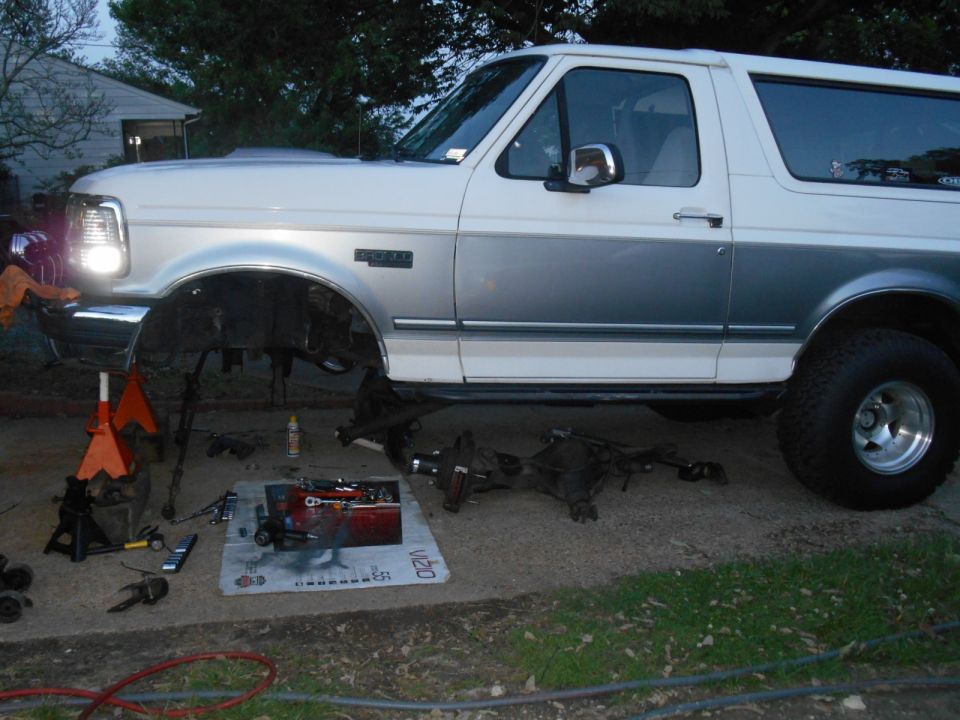 White and silver two-door SUV with front end on jack stands, front axle removed.