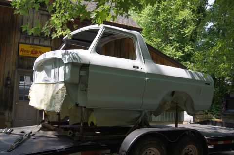 1979 Ford Bronco - A 1979 Ford Bronco body, primed in a light gray, is mounted on a trailer for transport. The vehicle is undergoing restoration, with masking…