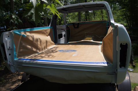 1979 Ford Bronco - The bed of a light-colored pickup truck is covered in brown paper and blue painter's tape, with a "Ford Service Parts" logo visible on the…