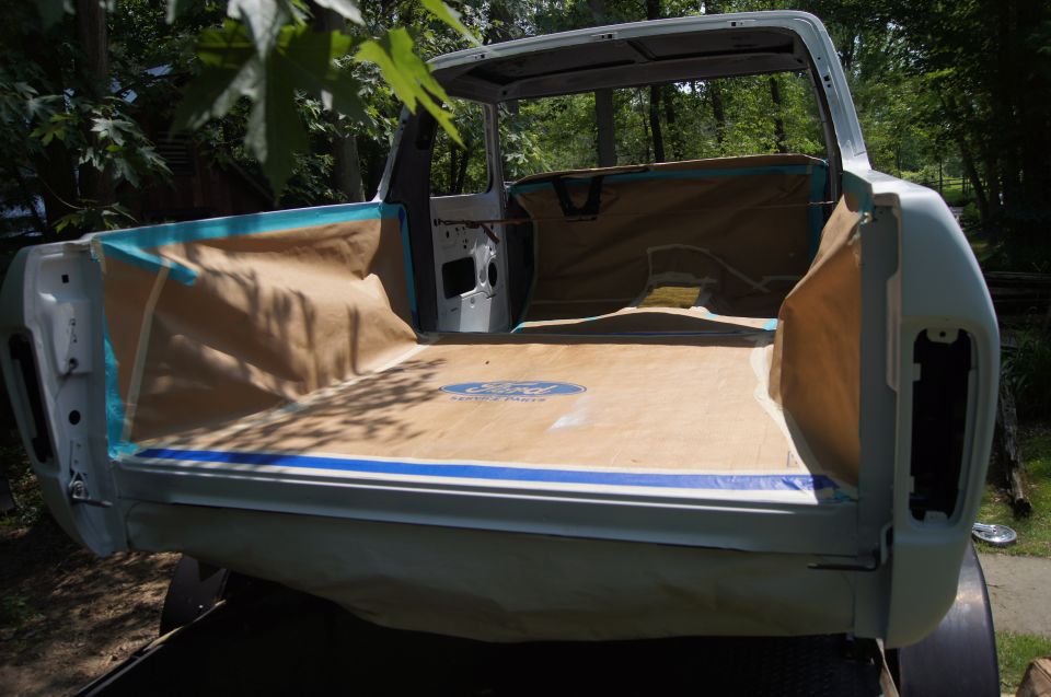Interior of a pickup truck bed covered in brown paper and blue tape, with a Ford logo.