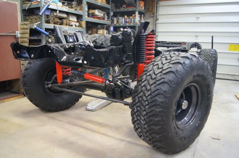 1979 Ford Bronco - The black frame and suspension of a vehicle, possibly a 1979 Ford Bronco, are shown in a workshop setting. It features large off-road tires…
