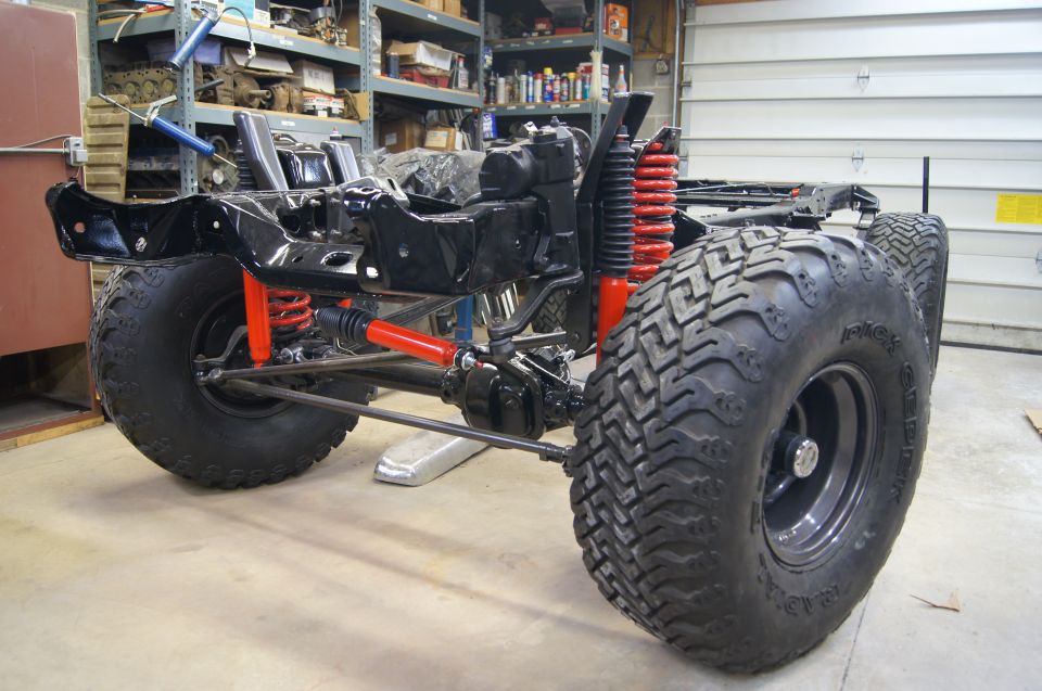 Black vehicle frame with red suspension components and large off-road tires in a workshop.
