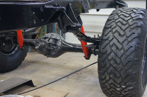 1979 Ford Bronco - Close-up view of the rear suspension and differential of a black vehicle, featuring red shock absorbers and a large, aggressive tire tread.