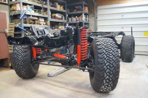 1979 Ford Bronco - The chassis and suspension of a vehicle, likely a 1979 Ford Bronco, are shown in a garage setting. The front suspension features bright red…