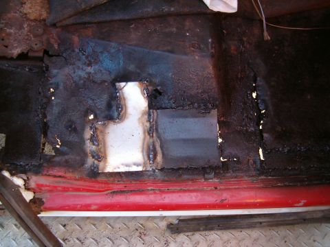 1979 Ford Bronco - Close-up of a heavily rusted vehicle floor pan with a newly welded patch panel.