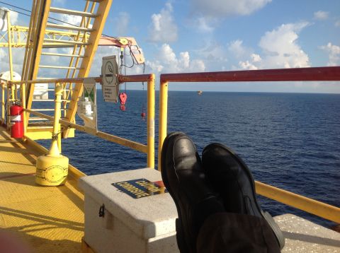1992 Ford Bronco - A person's feet in black shoes are resting on a white box on an offshore platform. The ocean and sky are visible in the background.
