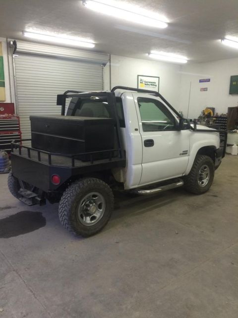 1985 Jeep CJ7 - A white pickup truck with a flatbed and a black toolbox is parked inside a garage. The truck has a custom headache rack and large off-road…