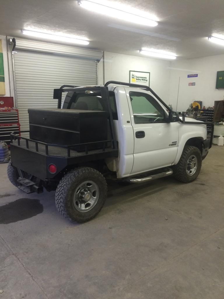 White pickup truck with flatbed and toolbox in a garage.