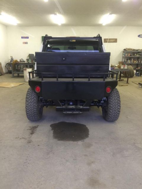 1985 Jeep CJ7 - The rear view of a modified Jeep CJ7 with a custom black flatbed and toolboxes is shown in a garage setting. The vehicle has large off-road…