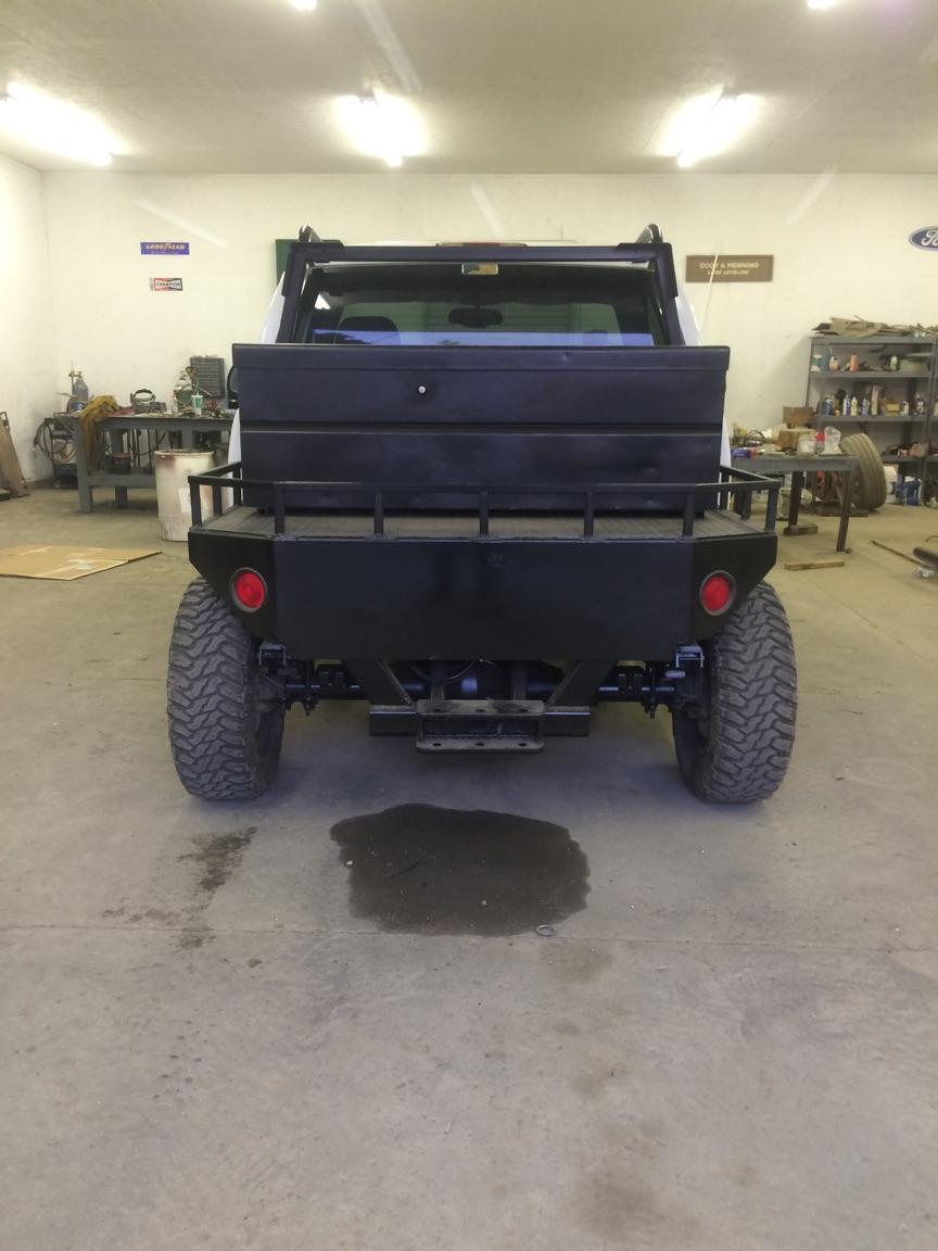 Rear view of a black custom Jeep CJ7 flatbed with off-road tires in a garage.