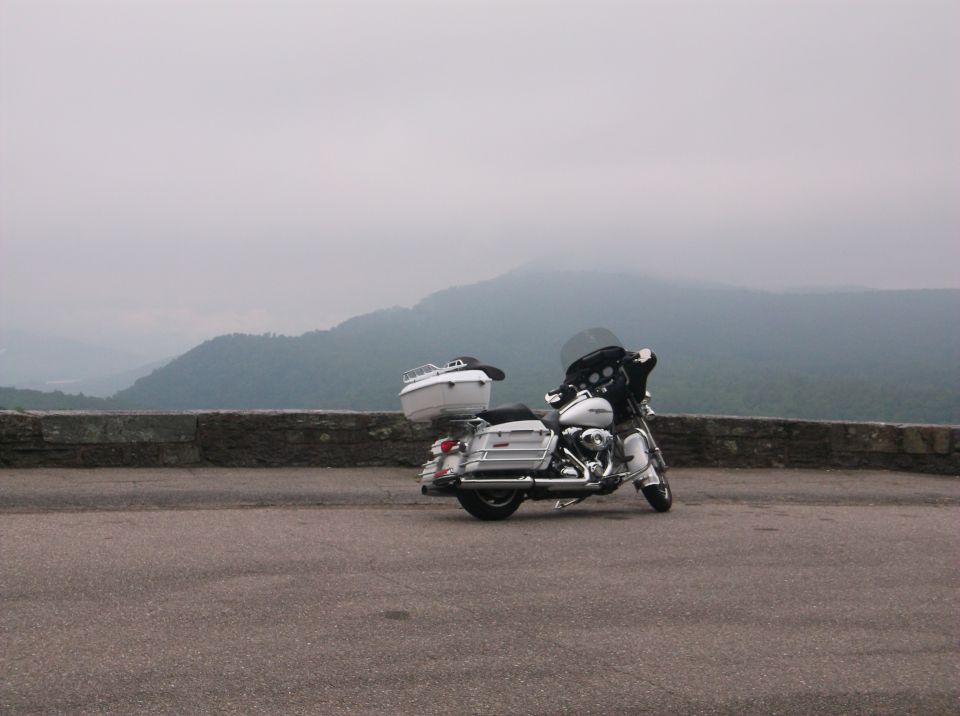 Silver Harley-Davidson touring motorcycle parked on a scenic overlook with misty mountains in the background.